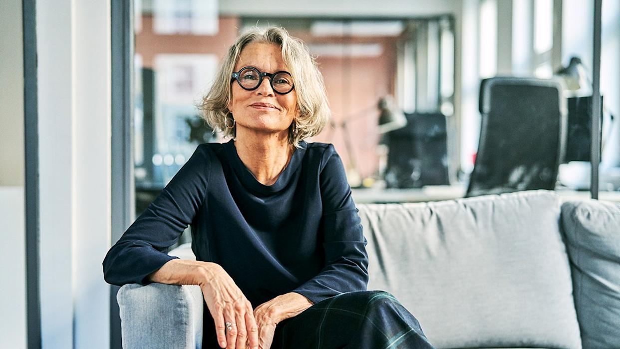 Portrait of a confident senior businesswoman sitting on a sofa in an office lobby, looking at the camera with a warm and professional smile