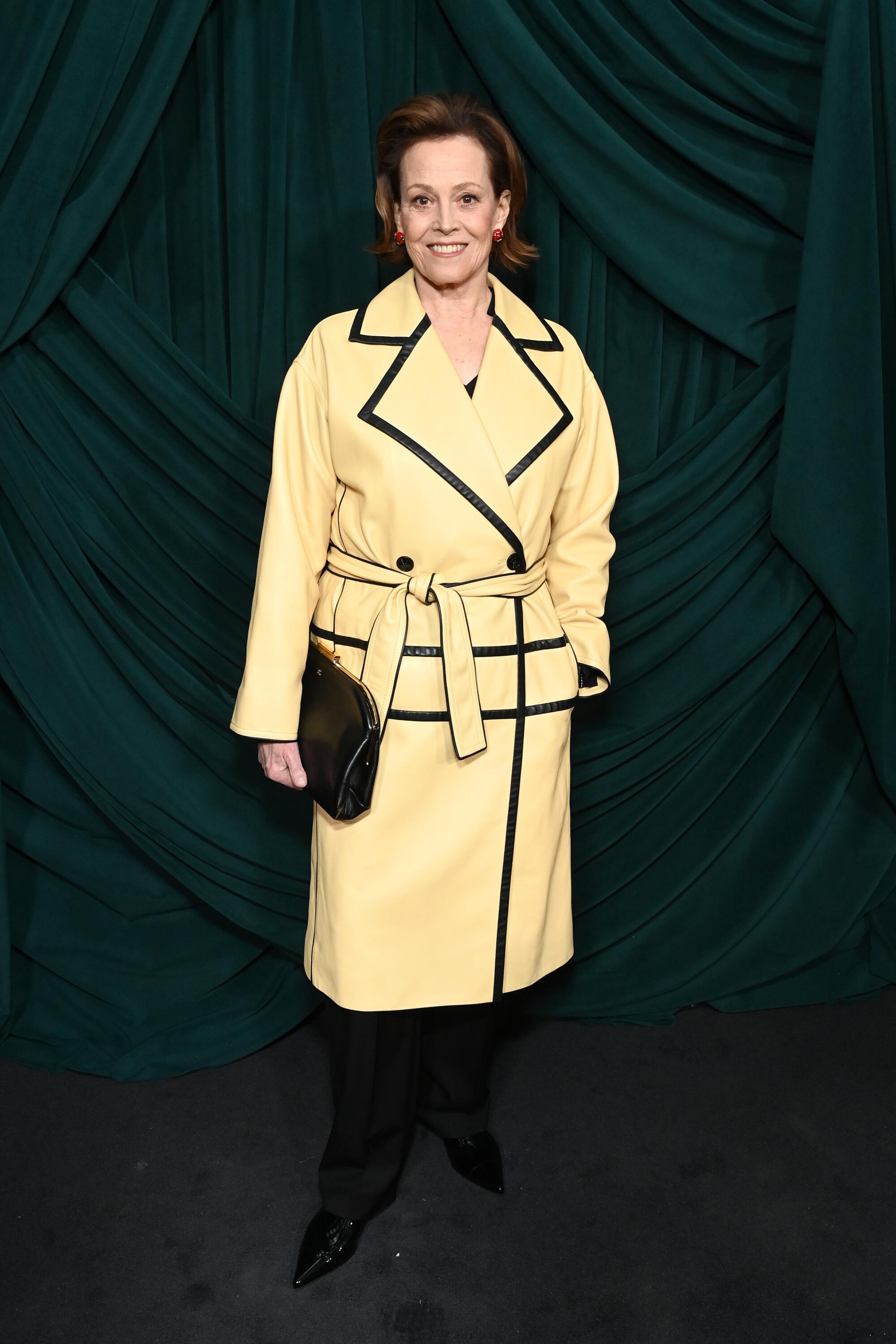 A woman poses in a tan jacket with black trim