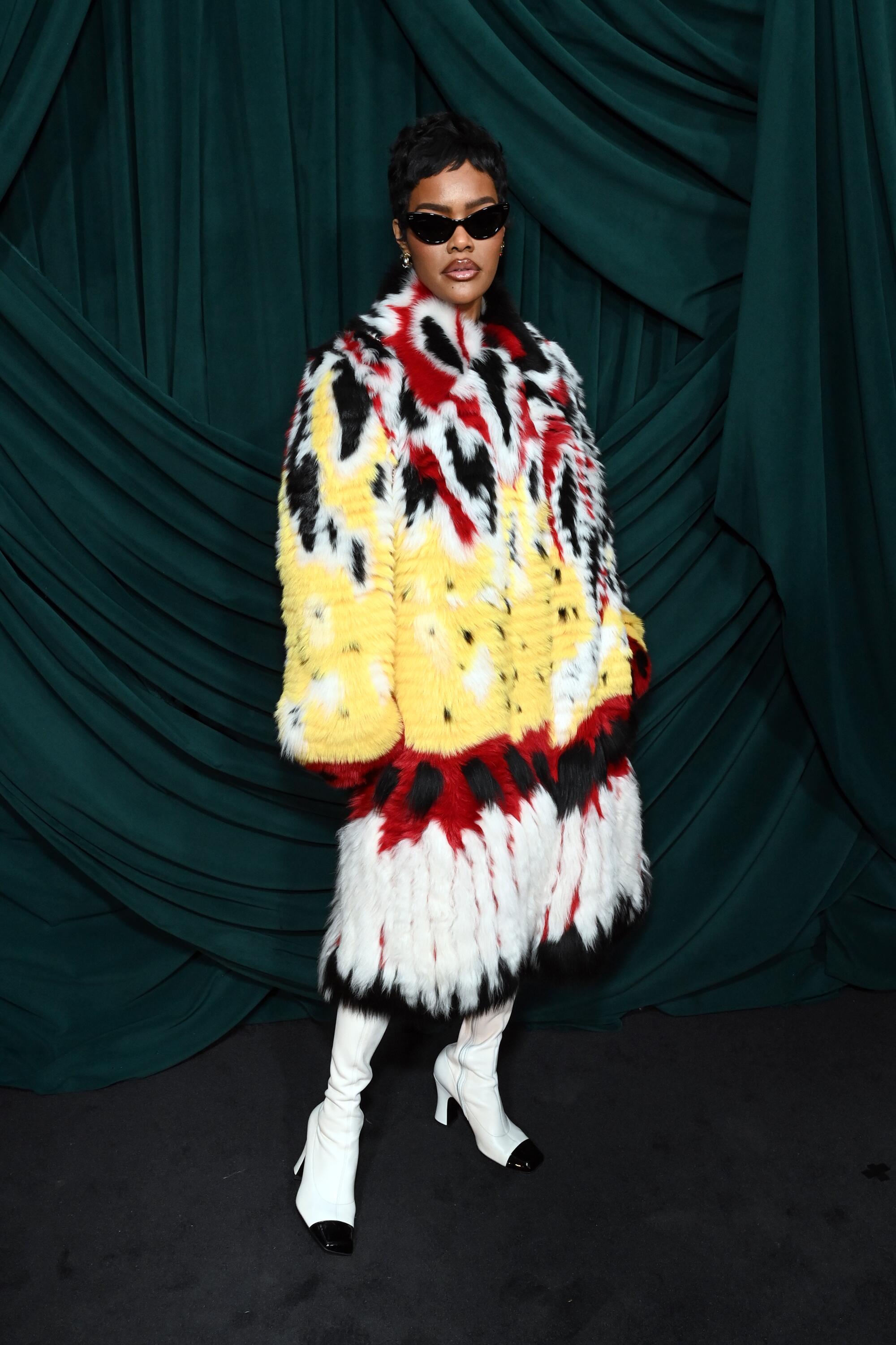 a woman poses in a colorful jacket and sunglasses