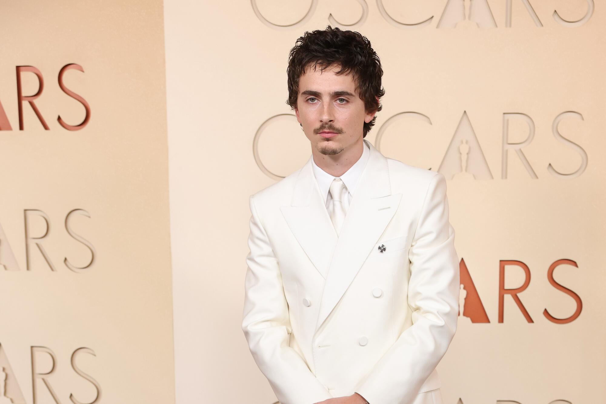 Timothée Chalamet, in an all-white suit, poses on the red carpet. 