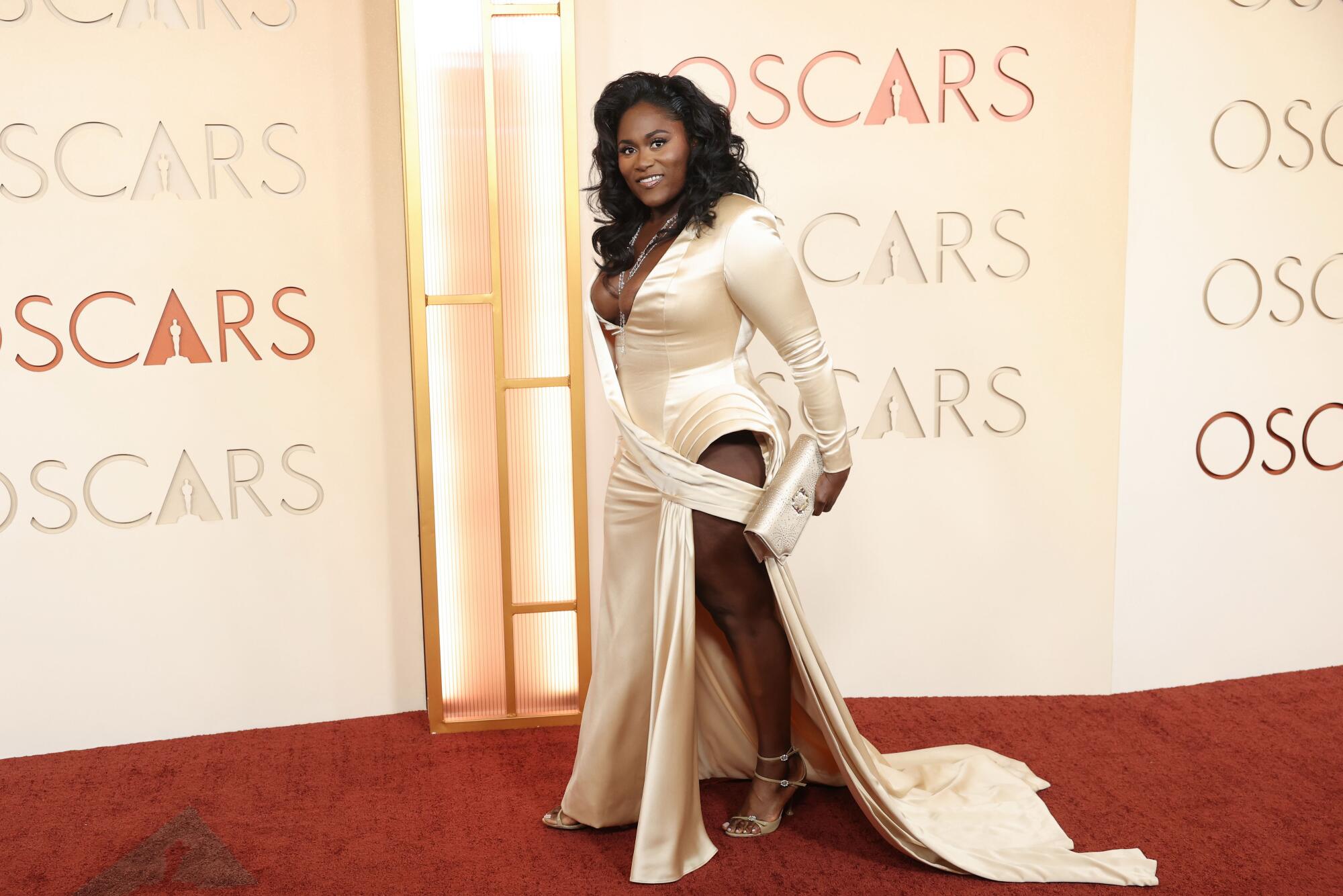 Danielle Brooks, wearing a Champagne dress with a high slit, walks the red carpet. 