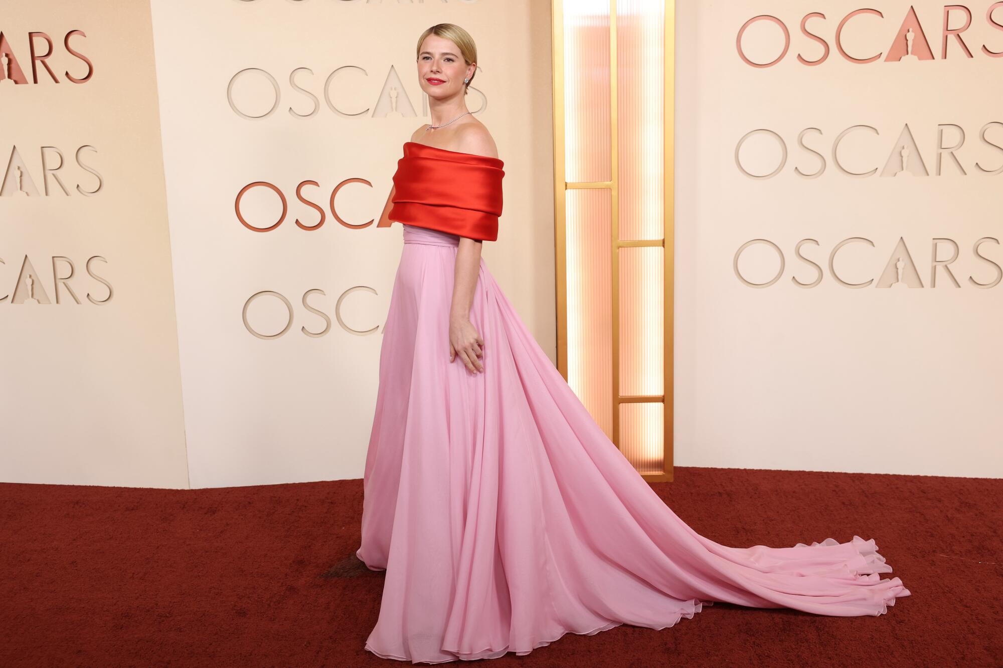 Jessie Buckley, wearing a red and pink chiffon gown, poses on the red carpet. 
