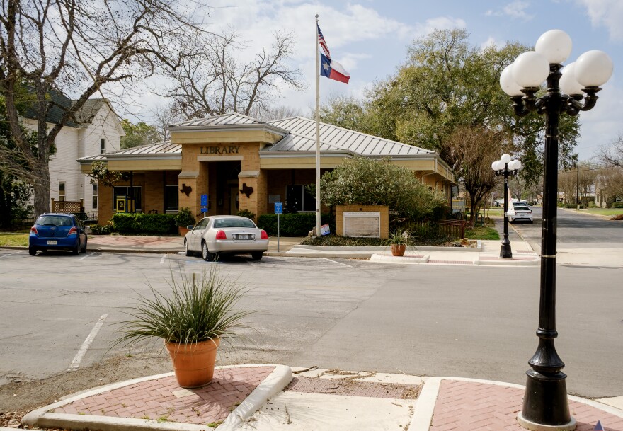 The Smithville Public Library sits across a street with a U.S. flag flying in front of it. In the foreground is a potted plant and a lamp post. 