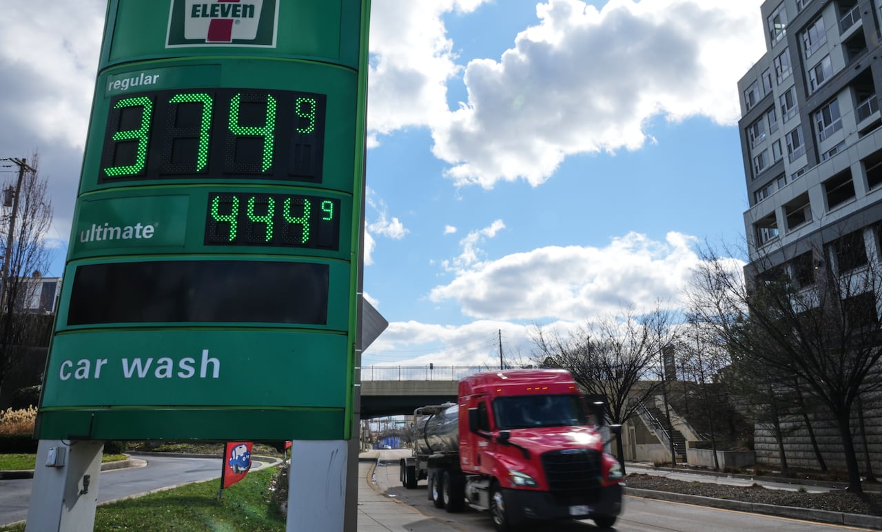 A truck drives past a 7-Eleven service station sign showing a price of $3.749 for a gallon of regular gas. 