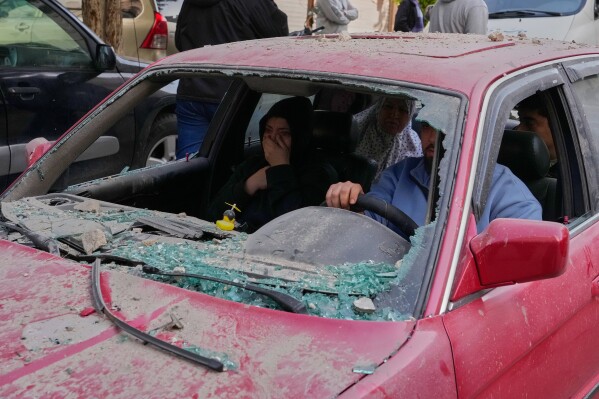 Family members in a damaged car flee the site of an Israeli airstrike that hit an apartment building in the southern port city of Sidon, Lebanon, Friday, March 13, 2026. (AP Photo/Mohammed Zaatari)