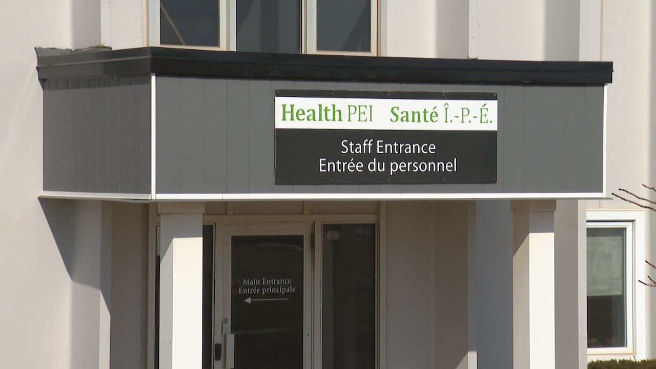 A white building is seen from its front with a white and black sign with green and white text.