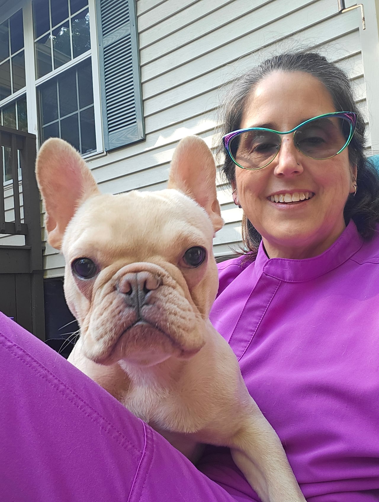 A woman wearing a brought purple outfit holds a small dog
