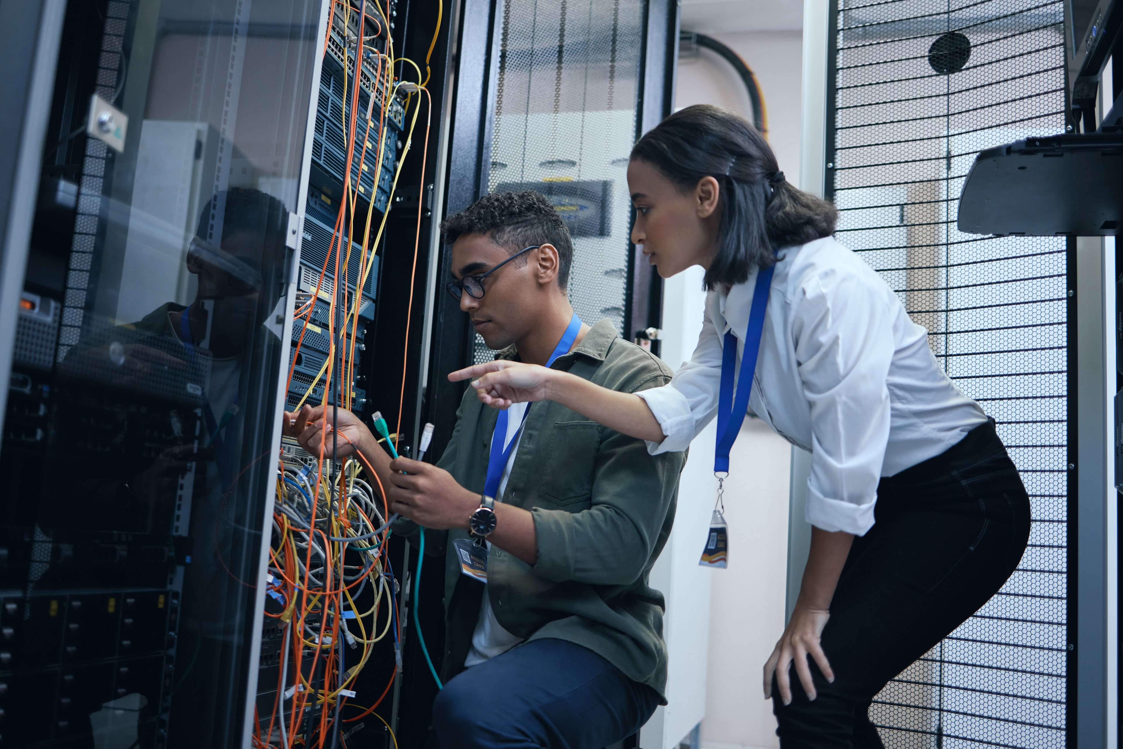 Two engineers checking wires and switches on a data center server tower.