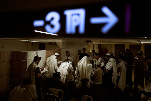 Jewish men wrapped in prayer shawls pray in an underground parking garage used as a shelter against possible Iranian missile attacks in Tel Aviv, Israel, Tuesday, March 3, 2026. (AP Photo/Oded Balilty)