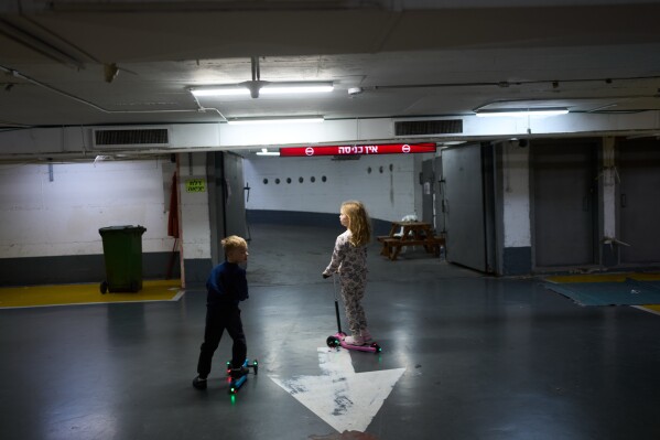 Children play in an underground parking garage where people spend the night as a precaution against possible Iranian missile attacks in Tel Aviv, Israel, Saturday, March 14, 2026. (AP Photo/Oded Balilty)