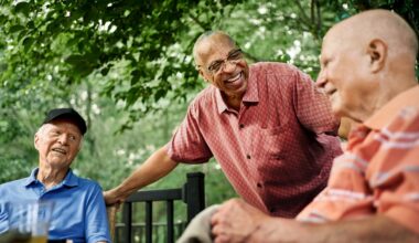 Group of happy senior male residents gathered around a table in the backyard of a retirement home, engaging in conversation and enjoying the serene outdoor space.