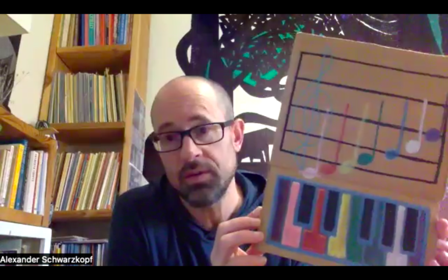 Man holding up a cardboard cutout with a drawing of colorful piano keys. 