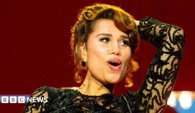 Raye smiles as she performs on stage in a black ballgown