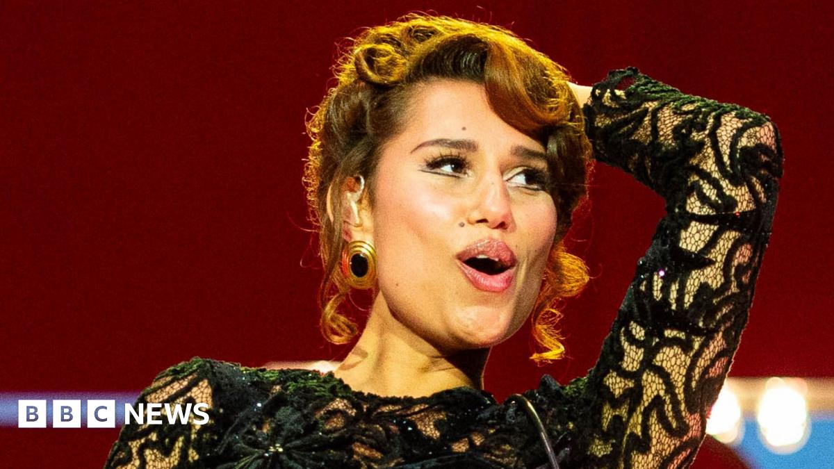 Raye smiles as she performs on stage in a black ballgown