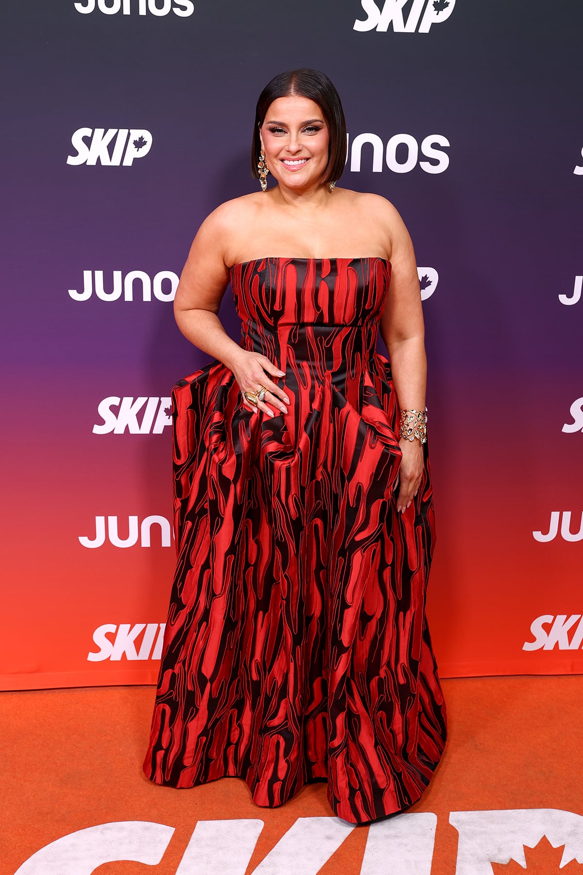 A woman poses for photos on a carpet wearing a strapless gown.
