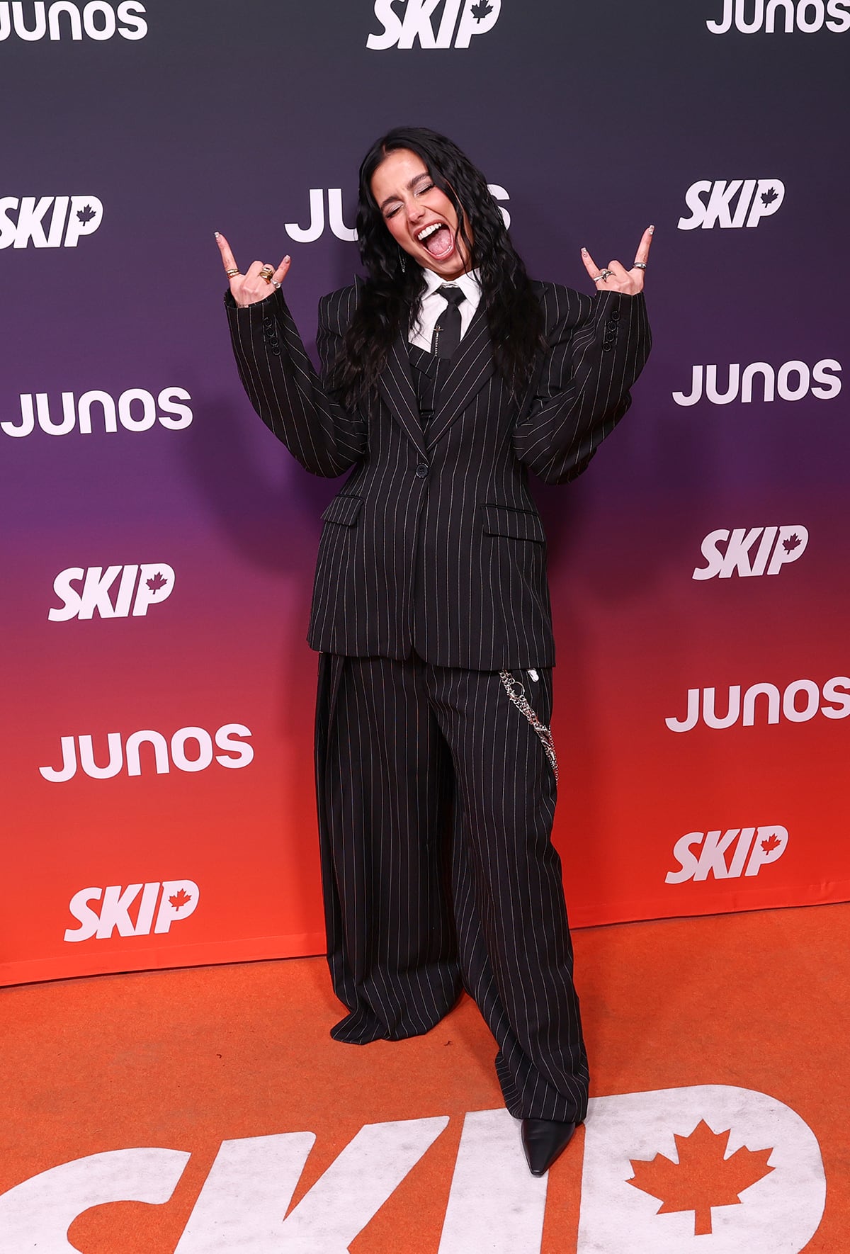 A woman poses throwing devil-horn hands up and wearing an oversized, wide-leg pinstripe suit.