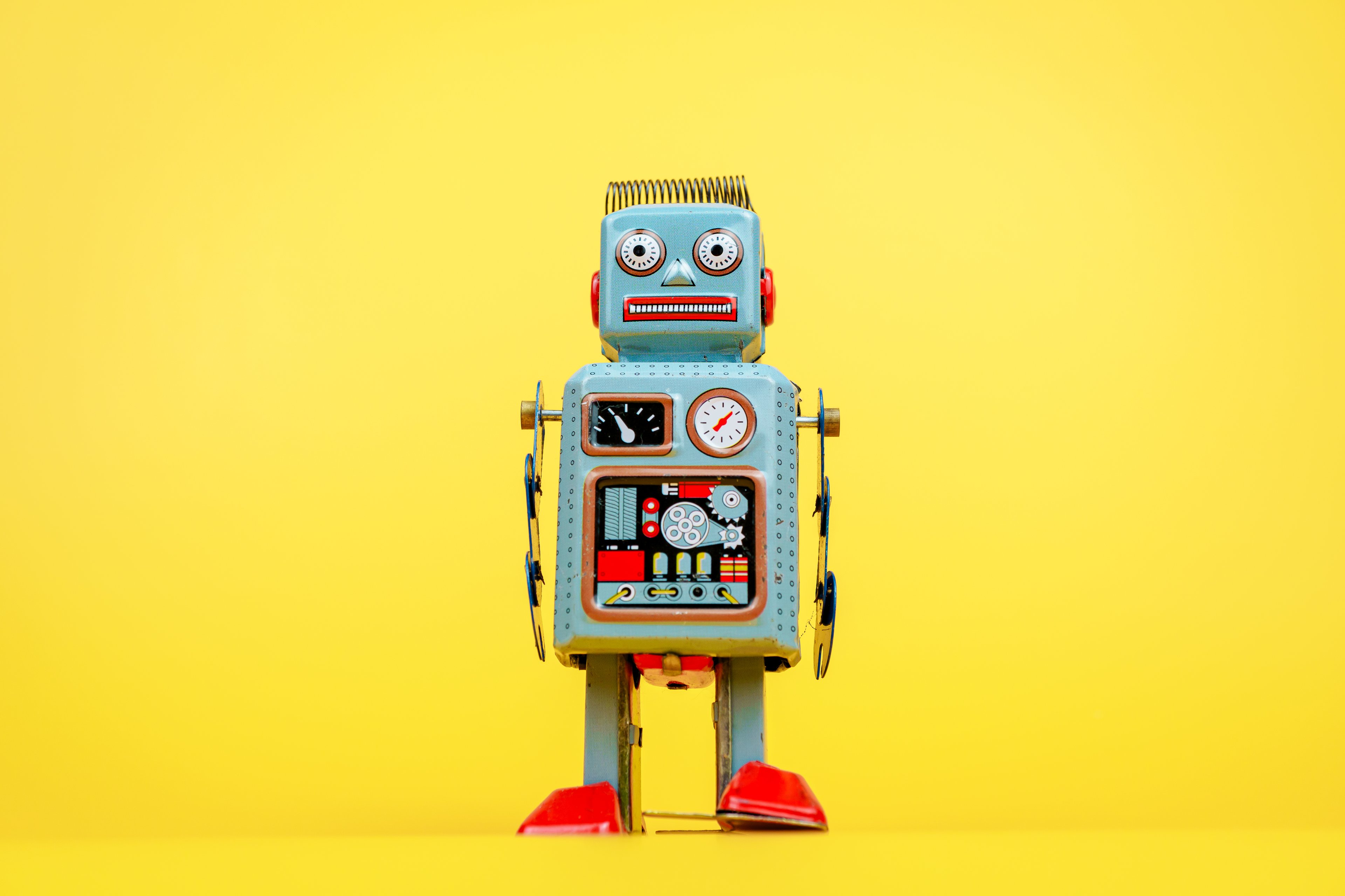 A robot looks at the camera. Yellow background.
