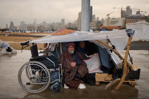 A man with his wife, displaced from Beirut's southern suburb of Dahiyeh, shelter from the rain inside a tent along the coast in Beirut, Lebanon, Thursday, March 26, 2026. (AP Photo/Emilio Morenatti)