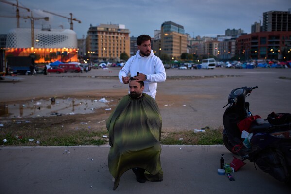 Hussein gets a haircut from Hassan in an open field where people who fled Israeli strikes in southern Lebanon have set up tents as shelters, in Beirut, Lebanon, Wednesday, March 25, 2026. (AP Photo/Emilio Morenatti)