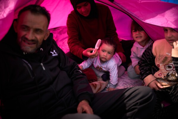 Members of the displaced Abd el-Hajj family, and two of their cousins, right, who fled Israeli strikes in southern Lebanon, sit inside a tent used as a shelter in Beirut, Lebanon, Wednesday, March 25, 2026. (AP Photo/Emilio Morenatti)