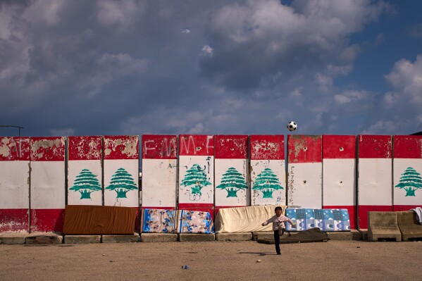 A boy, displaced with his family from Beirut's southern suburbs of Dahiyeh, plays with a ball next to rain-soaked mattresses drying in the sun in Beirut, Lebanon, Friday, March 27, 2026. (AP Photo/Emilio Morenatti)