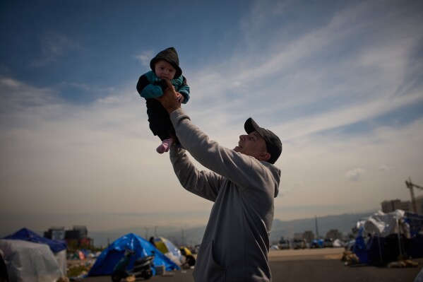 Abed Driss, displaced with his family from Beirut's southern suburbs of Dahiyeh, holds up his son Benin, 3 months, next to a tent used as a shelter in Beirut, Lebanon, Saturday, March 28, 2026. (AP Photo/Emilio Morenatti)