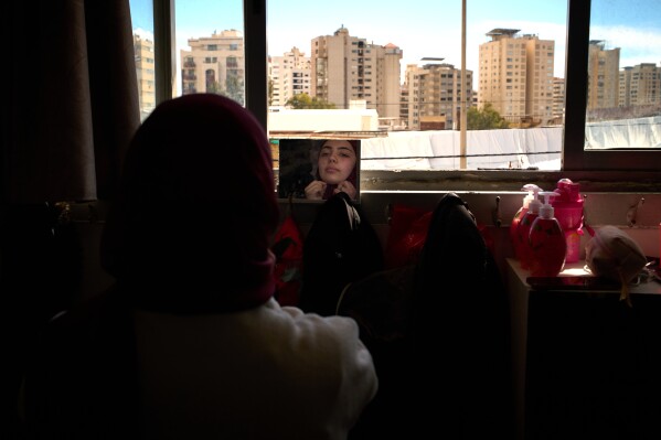Nour Zahraa Almokdad, 19, displaced from Beirut's southern suburb of Haret Hreik, adjusts her veil in front of a mirror in a school used as a shelter in Beirut, Lebanon, Wednesday, March 25, 2026. (AP Photo/Emilio Morenatti)