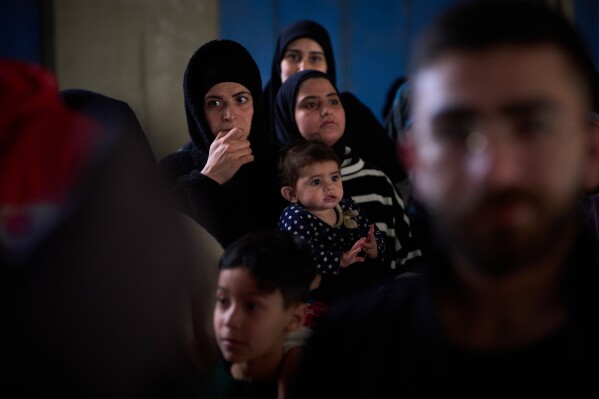 Displaced women with their children from Beirut's southern suburbs, wait to receive donated food rations inside a school converted into a shelter in Beirut, Lebanon, Friday, March 27, 2026. (AP Photo/Emilio Morenatti)