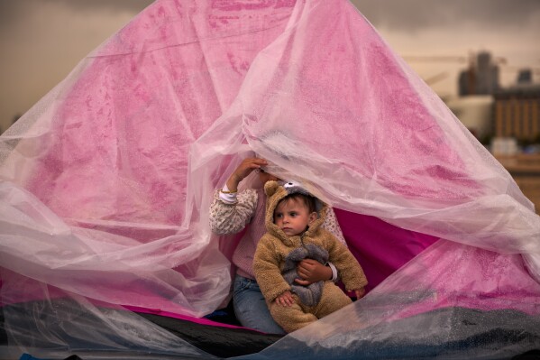 Yasmin holds her brother Ali, both displaced from Beirut's southern suburb of Dahiyeh, as they shelter from the rain inside a tent along the coast in Beirut, Lebanon, Thursday, March 26, 2026. (AP Photo/Emilio Morenatti)