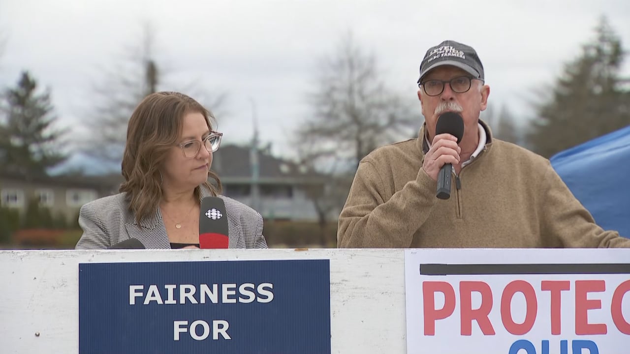 A man speaks into a microphone beside a woman standing behind a signs at a rally.