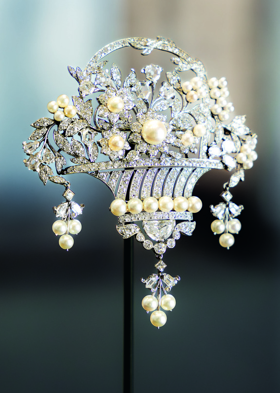 Vintage pearl and diamond brooch in an intricate floral basket design displayed against a blurred background.