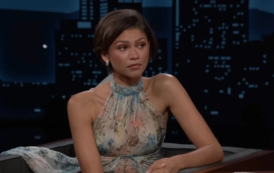 Person in floral halter dress appears thoughtful during a talk show interview