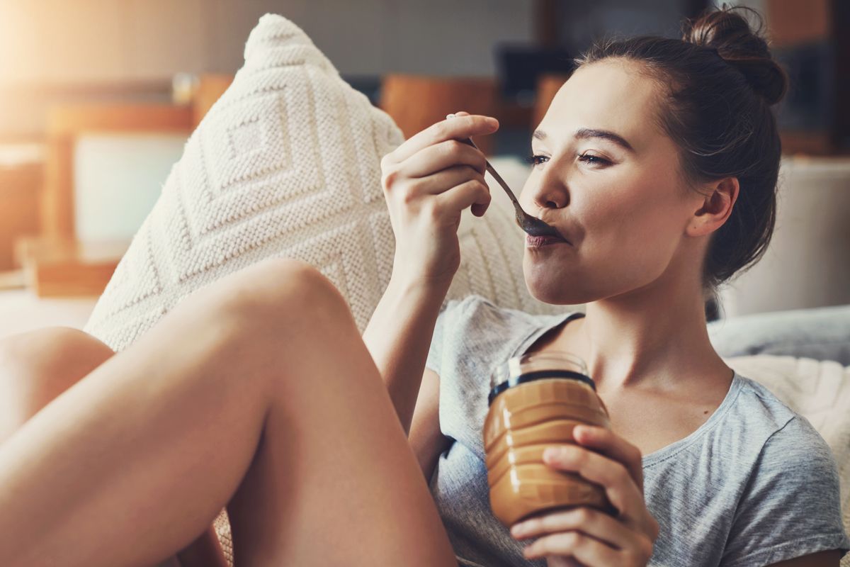 Woman on couch eating peanut butter from the spoon