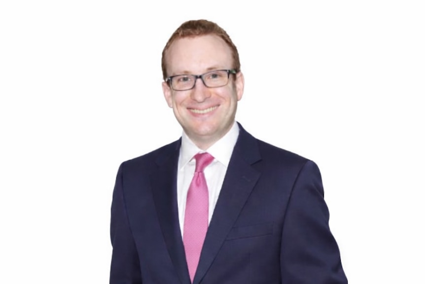 Man in suit smiles at camera in front of white background