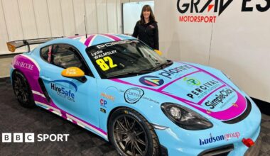 Lydia Walmsley dressed in all black stands in a car show room with her blue Porsche.