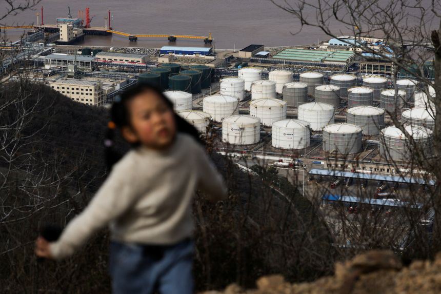 A child walks along a hiking trail with oil storage tanks and facilities of CNOOC Ningbo Daxie Petrochemical Co., Ltd. in the background in Ningbo, China, March 21, 2026.