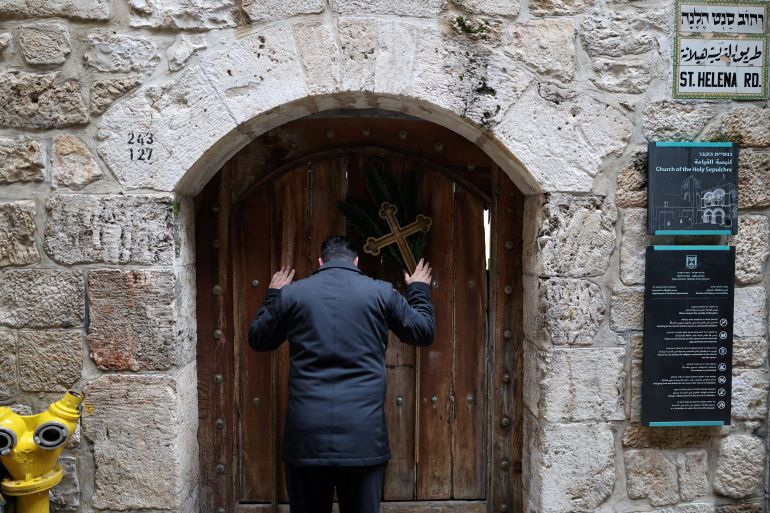 Palestinian Christian who is popular for being the Santa Claus of the city, holds a cross and a palm frond while standing at the doors of the Church of the Holy Sepulchre after finding them locked