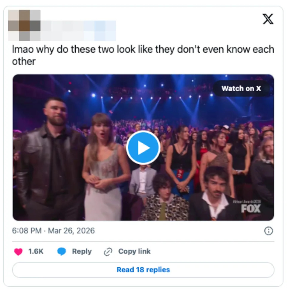 A man in a leather jacket and a woman in a sleeveless dress sit at an event. They look serious among a lively audience