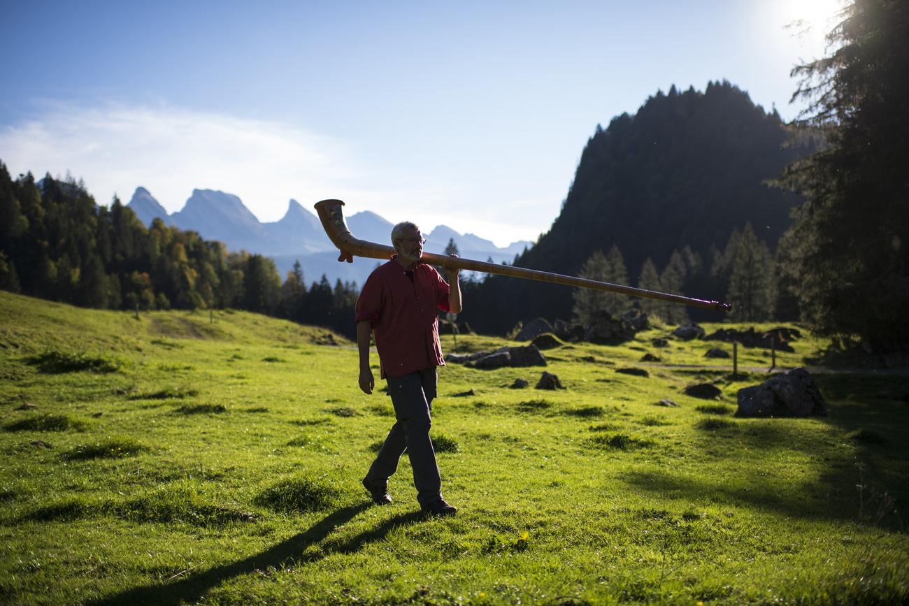 person walking in the mountains with an alpine horn on their shoulders