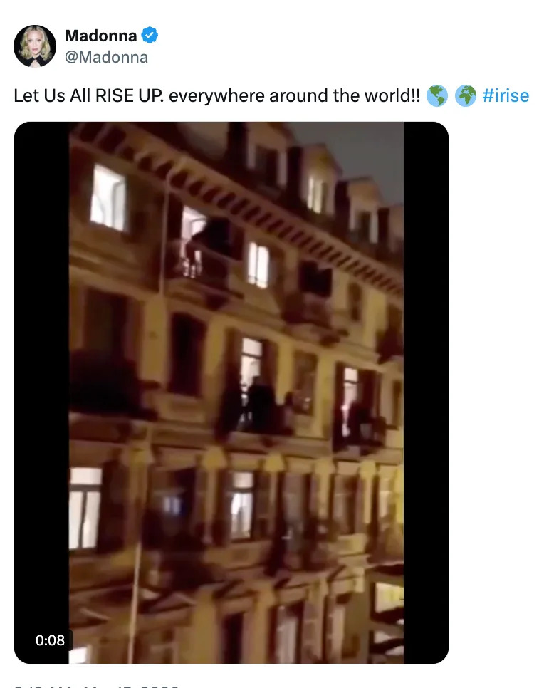 Video screenshot of people on balconies of an apartment building at night, with a tweet from Madonna above calling for unity
