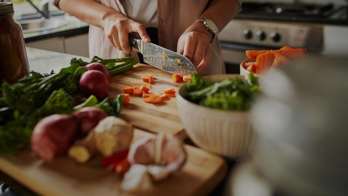 A woman is cutting vegetables on a wooden board.