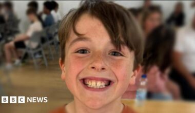 A boy called Rex is smiling at the camera - there are some people in the background of the photo