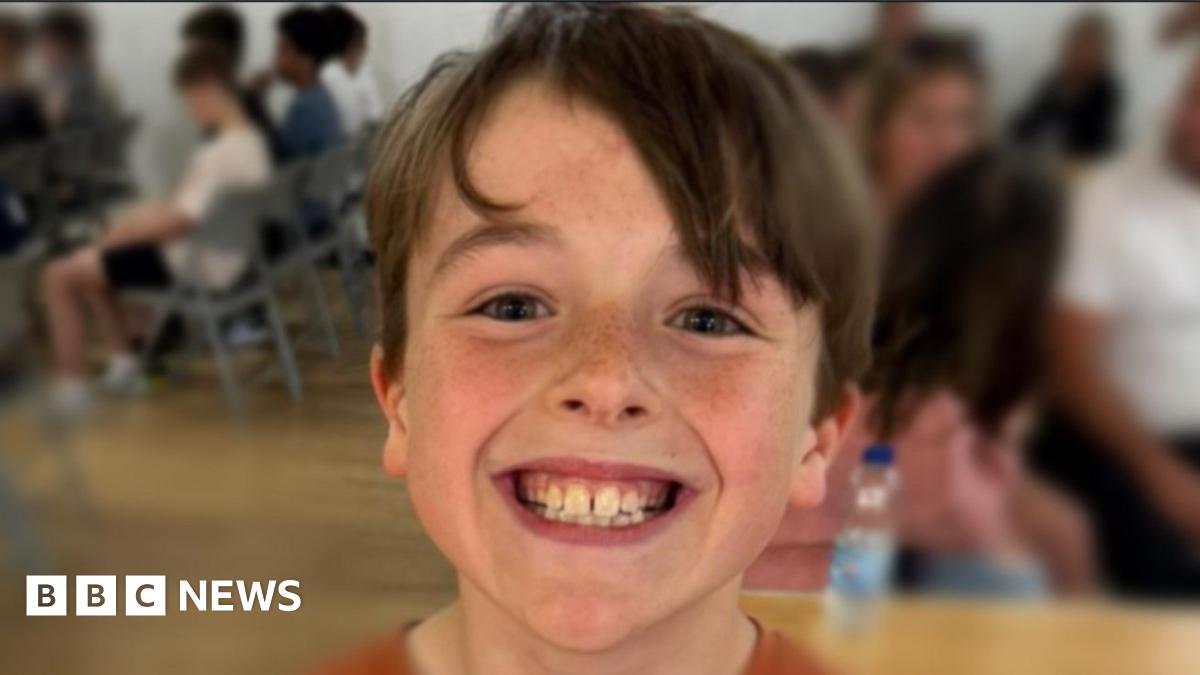 A boy called Rex is smiling at the camera - there are some people in the background of the photo