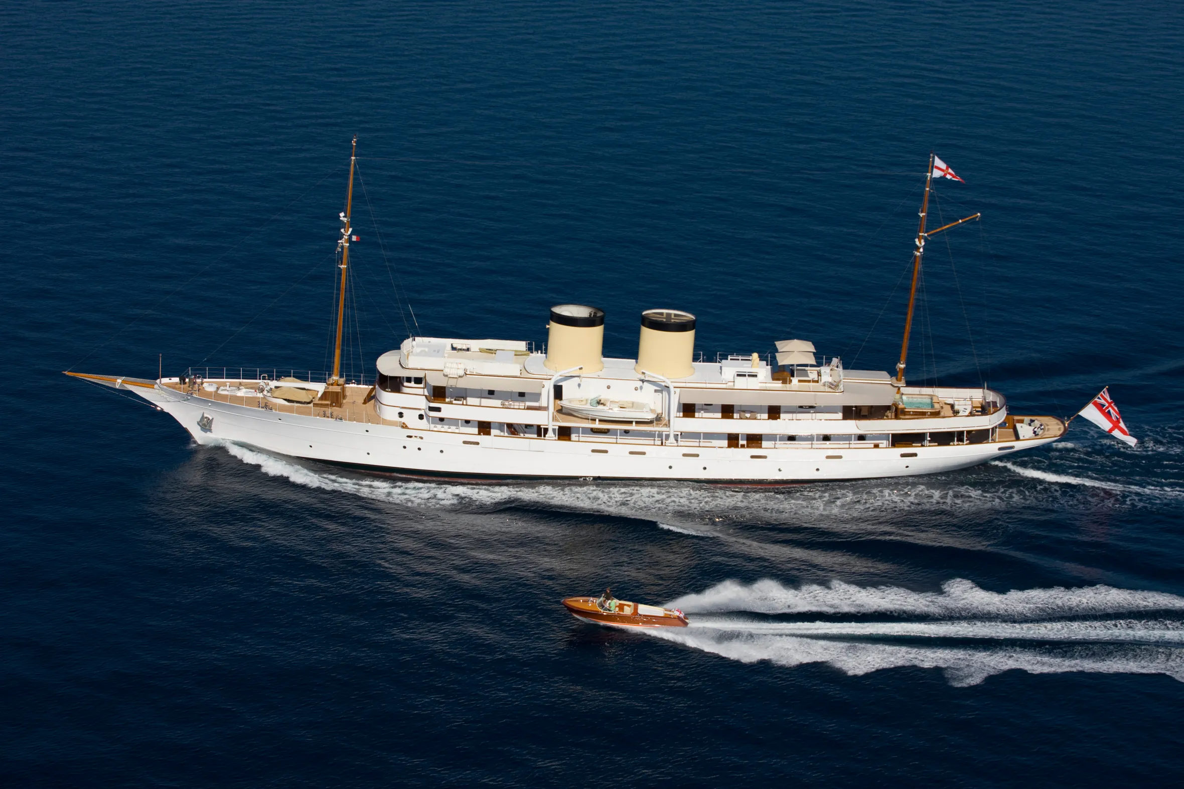 The yacht Talitha sailing in blue waters, with a smaller wooden boat moving alongside it.