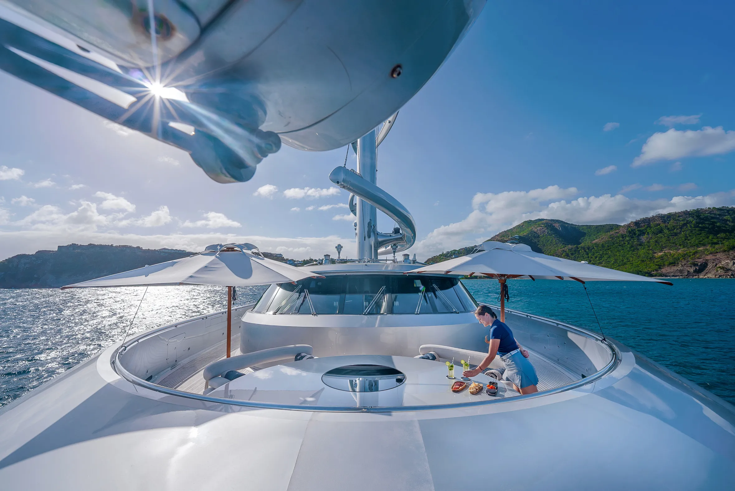 A woman arranging drinks and appetizers on an outdoor bar setup of the Jumeirah Maltese Falcon yacht.