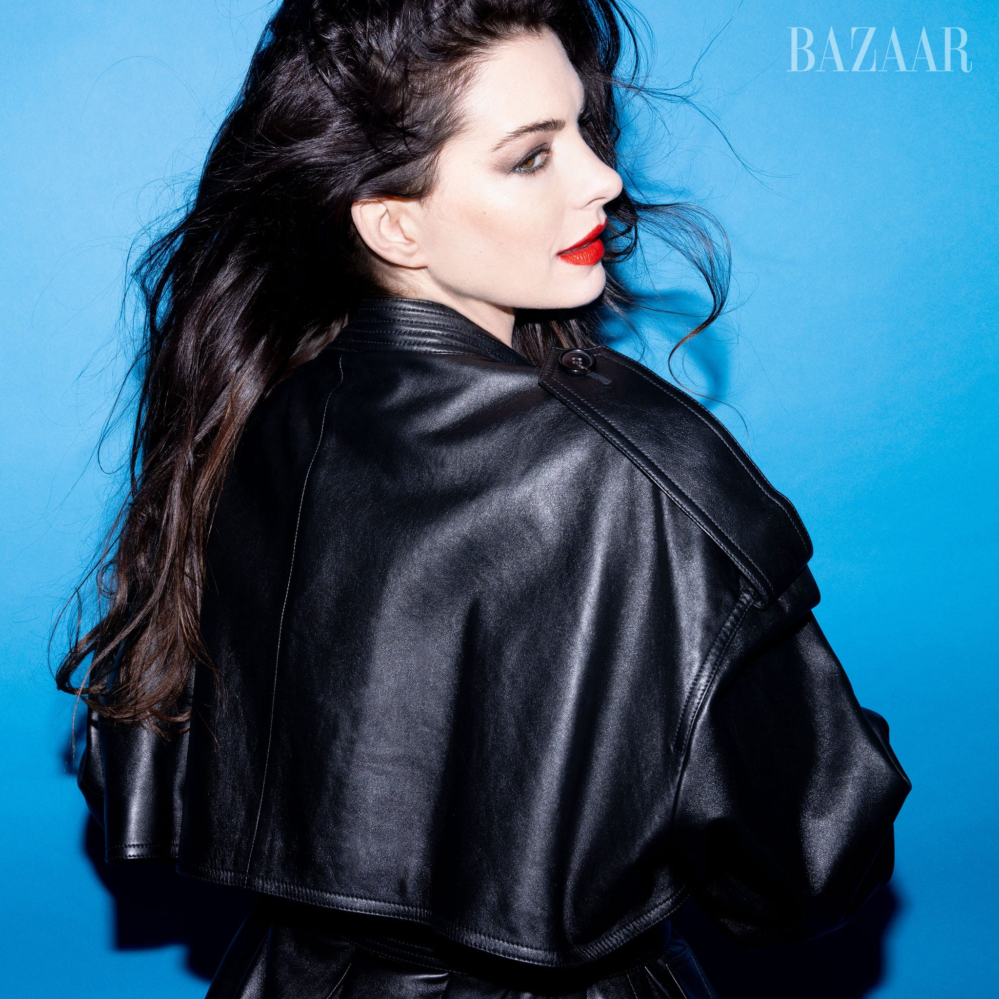 a person facing away with long dark hair wearing a black leather jacket against a blue background a person facing away with long dark hair wearing a black leather jacket against a blue background