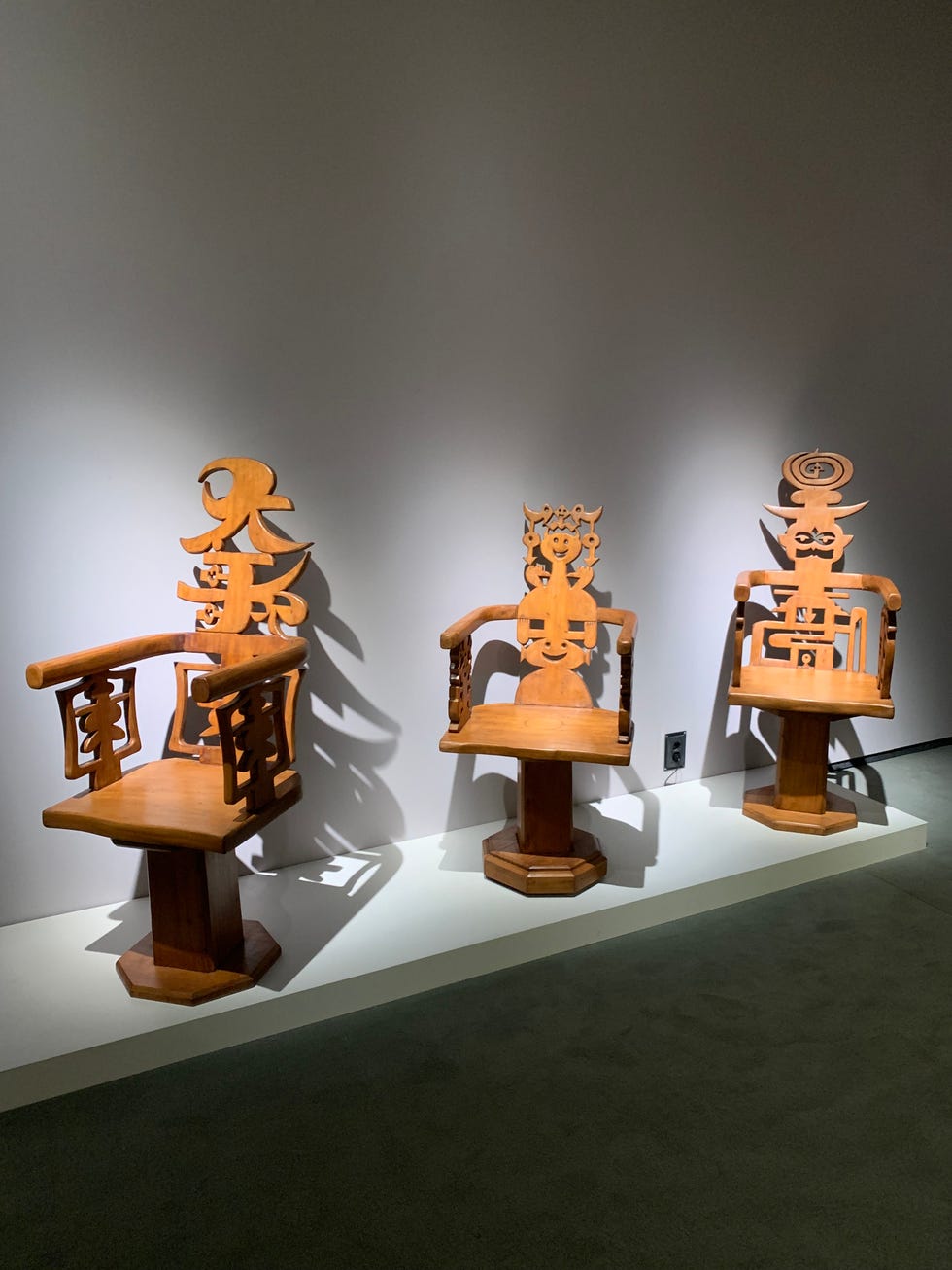 Three wooden chairs with unique symbolic designs.