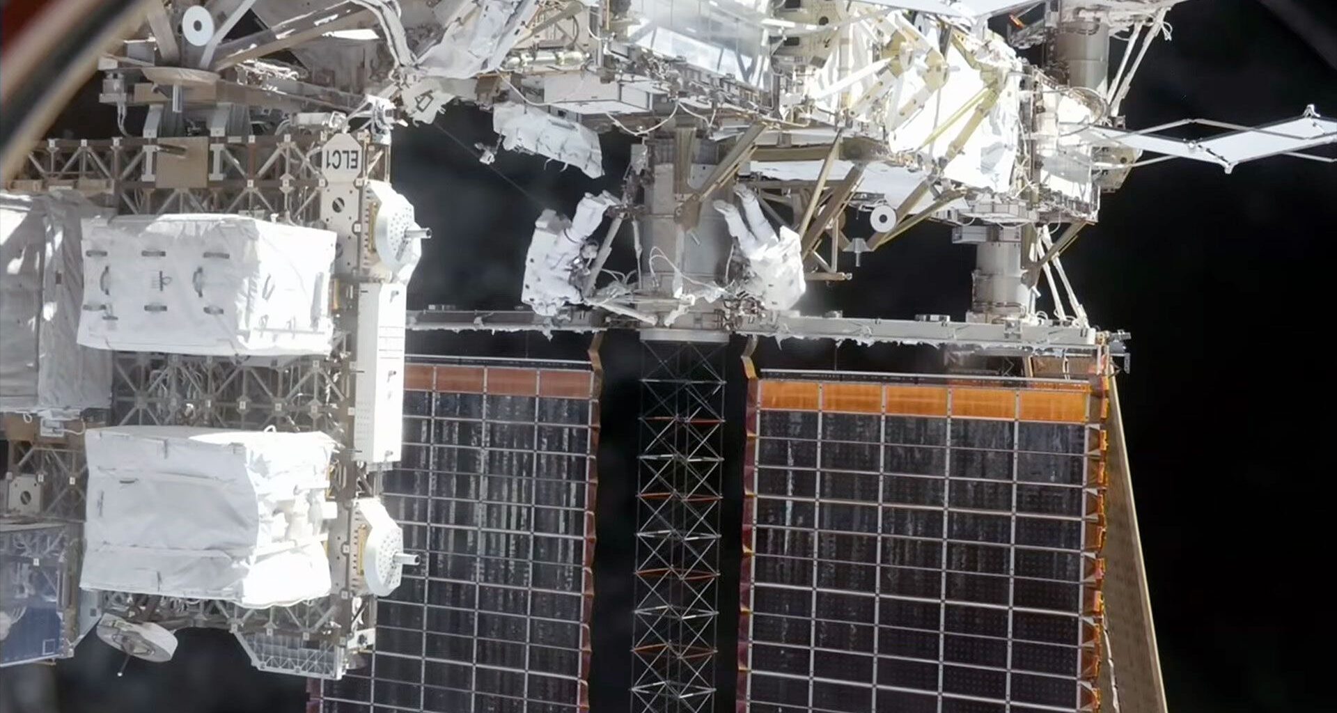 two astronauts wearing white spacesuits work outside of a space station "above" a pair of solar array panels