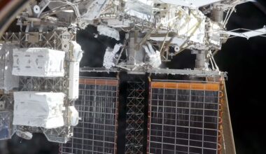 two astronauts wearing white spacesuits work outside of a space station "above" a pair of solar array panels
