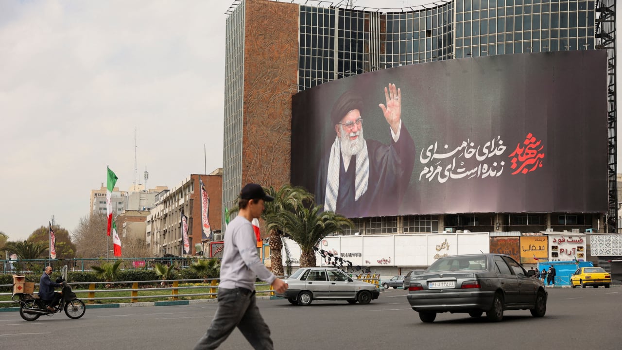 People walk near a billboard of Iran's late Supreme Leader Ayatollah Ali Khamenei on a street, after he was killed in Israeli and US strikes on Saturday, in Tehran, Iran, March 2, 2026